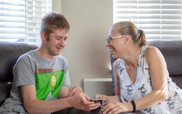 A service user and carer smile at a phone screen together