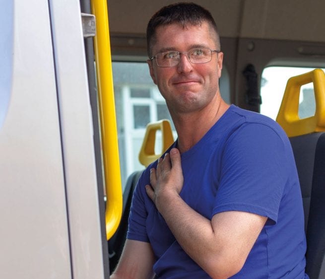 A Learning Disability service user smiles as he sits down on the mini bus