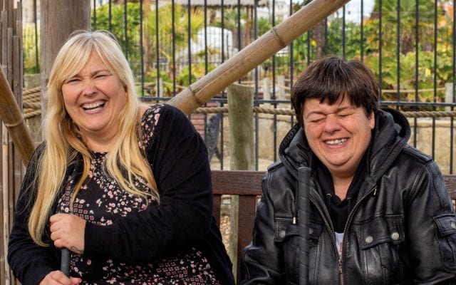 Two ladies from Ambient Support's Learning Disability services are laughing together, they are being supported on a day out. Supported living, short breaks, respite.