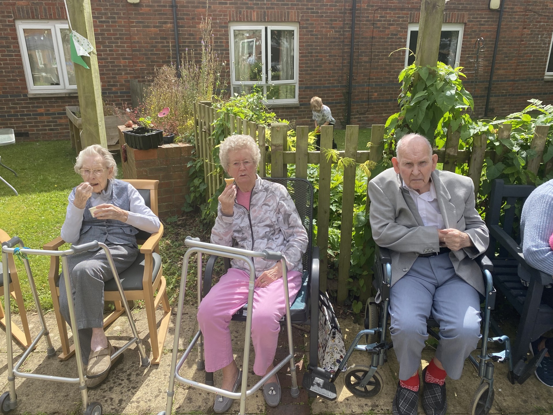 three older people, two ladies and a man are sitting down on chairs outside and eating an ice cream
